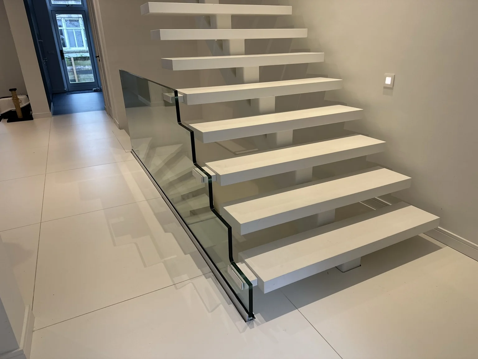 Detail van een glazen balustrade met uitsparingen langs witte traptreden