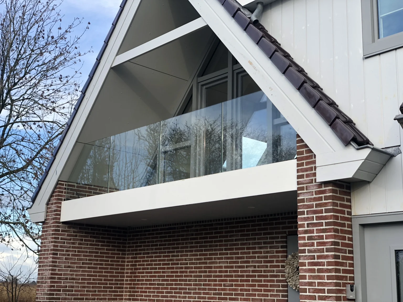 Glazen balkonbalustrade aan een woning met een puntdak