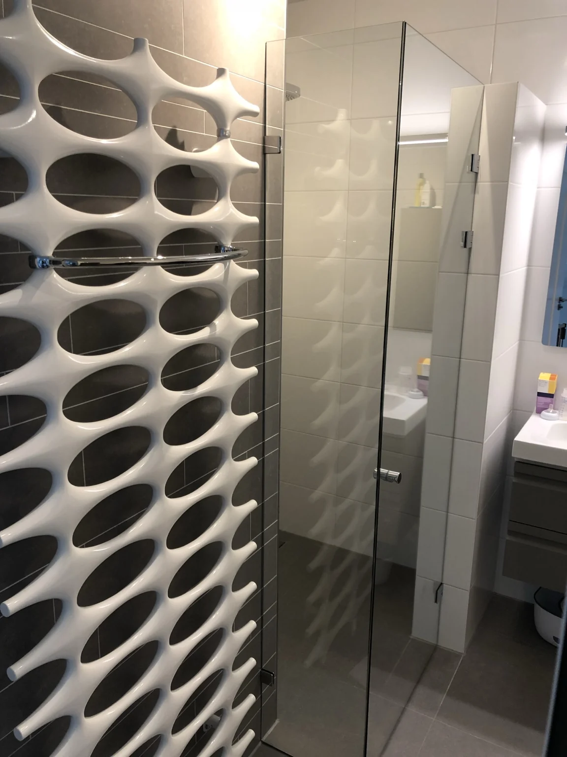 Glazen douchedeur naast een witte designradiator