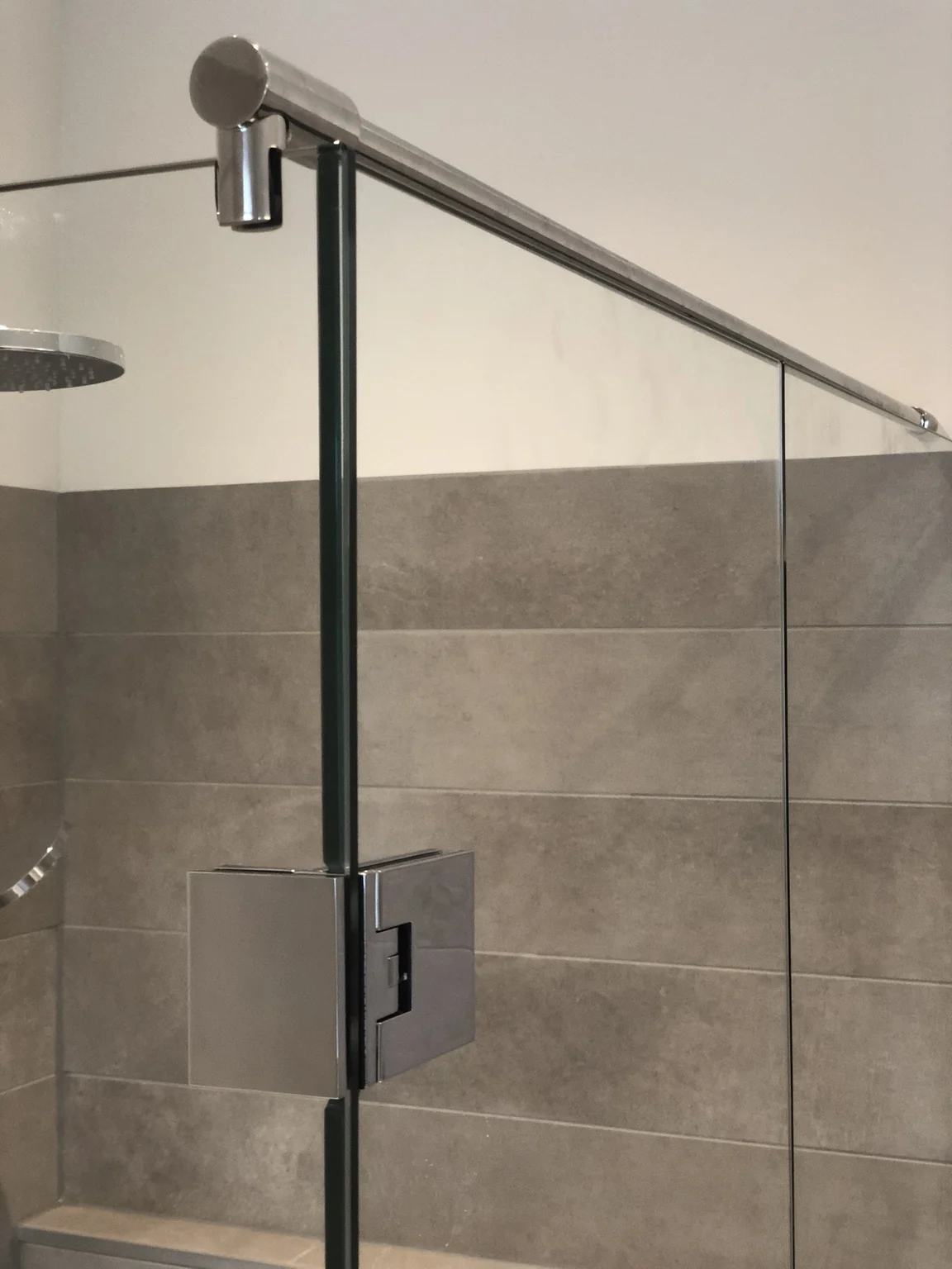 Detail van een glazen douchedeur met scharnier en stabilisatiestang