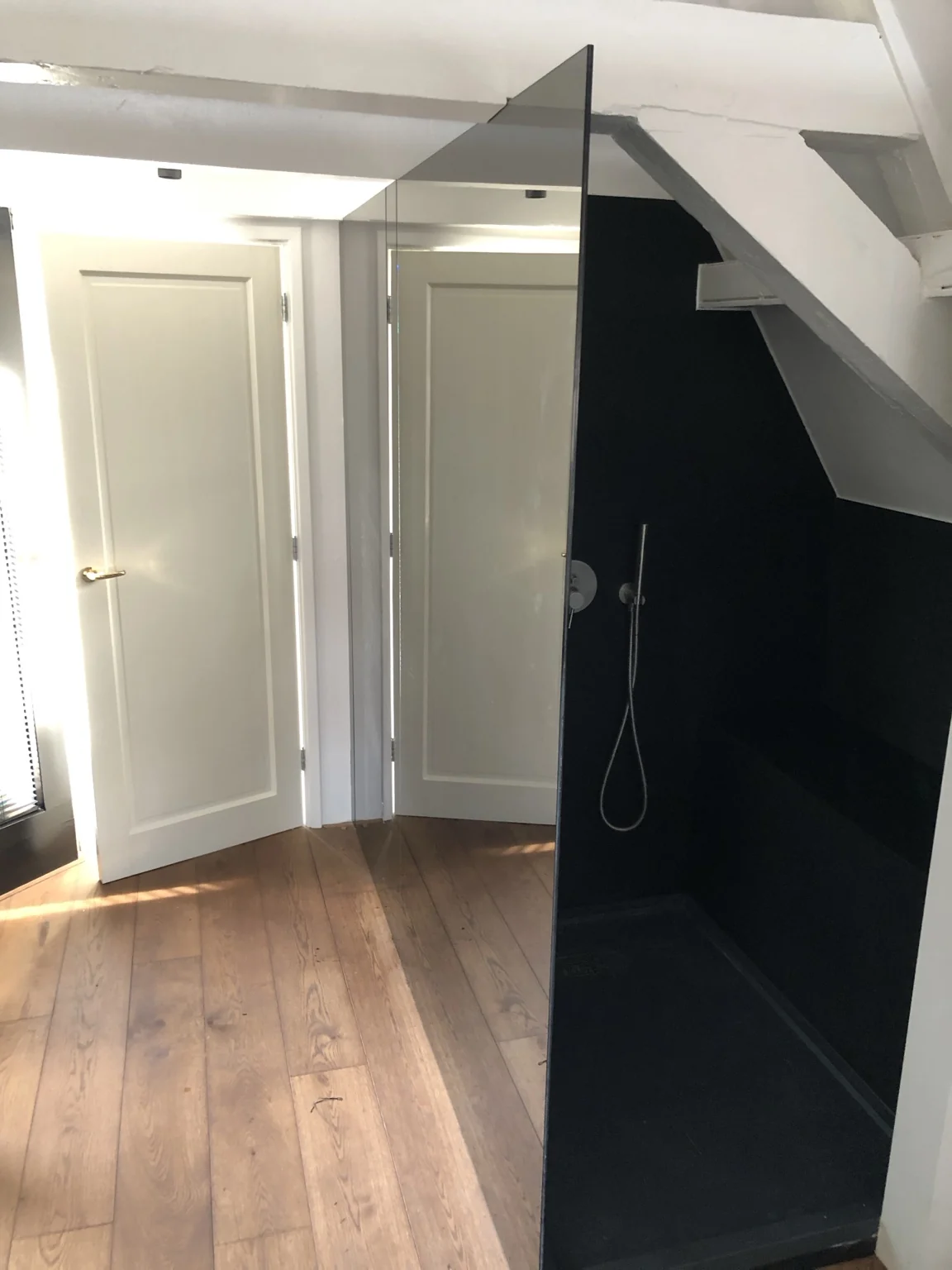 Glazen douchewand bij houten balken en een donkere douchewand