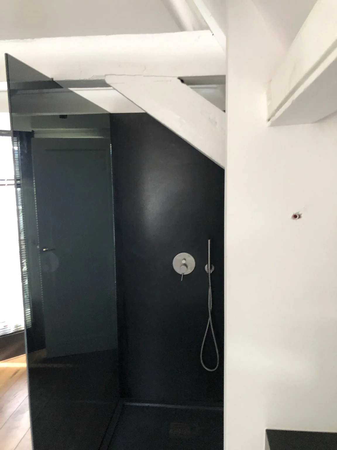 Glazen douchewand in een badkamer met een schuine houten balk